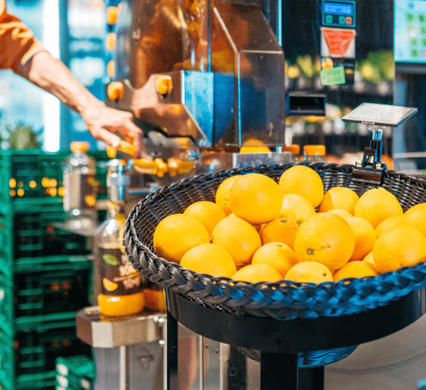 Corbeille remplie d'agrumes, par exemple d'oranges, positionnée à côté d'une centrifugeuse, présentée de manière attrayante et pratique.