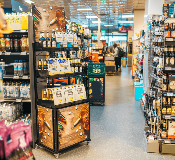 Zweit-Point-of-Sale mit drei Tablaren mit Display in Holzoptik Aufdruck "Getränke", auf jedem Tablar werden verschiedene Getränke, wie z.B alkoholfreies Bier ansprechend präsentiert.