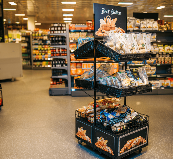 Zweiter Point of Sale Doppelseitig mit 6 Tablaren und Topper (Aufschrift Brot Station, Abbildung Brotkorb mit divers. Gebäck), auf den 6 Tablaren sind unterschiedliche Aufbackbrote präsentiert.